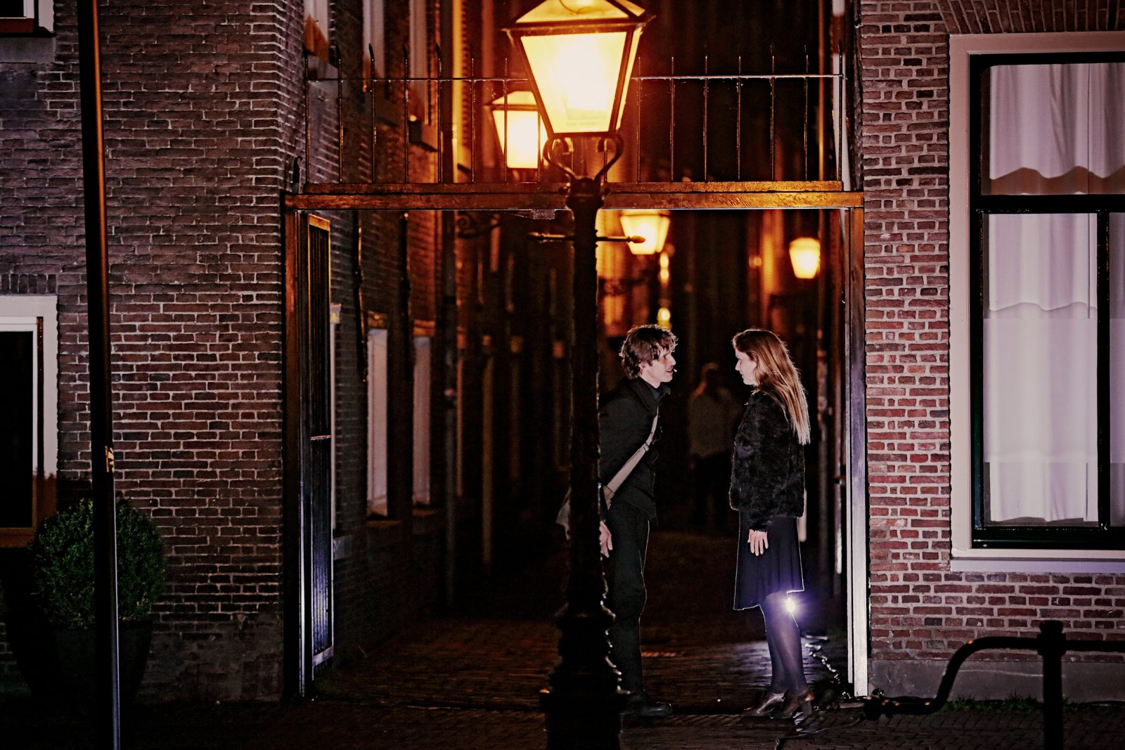 Twee spelers onder een lantaarn in een grachtenstraat bij nacht